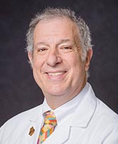 The image features a smiling man wearing a white lab coat, standing against a neutral background, with no visible text or distinguishing marks indicating his identity or profession.